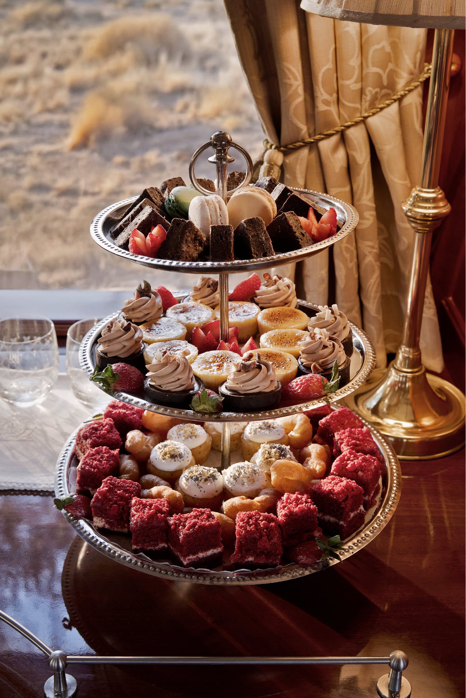 Etageré mit feinen Desserts und Gebäck im Rovos Rail vor der vorbeiziehenden afrikanischen Landschaft.