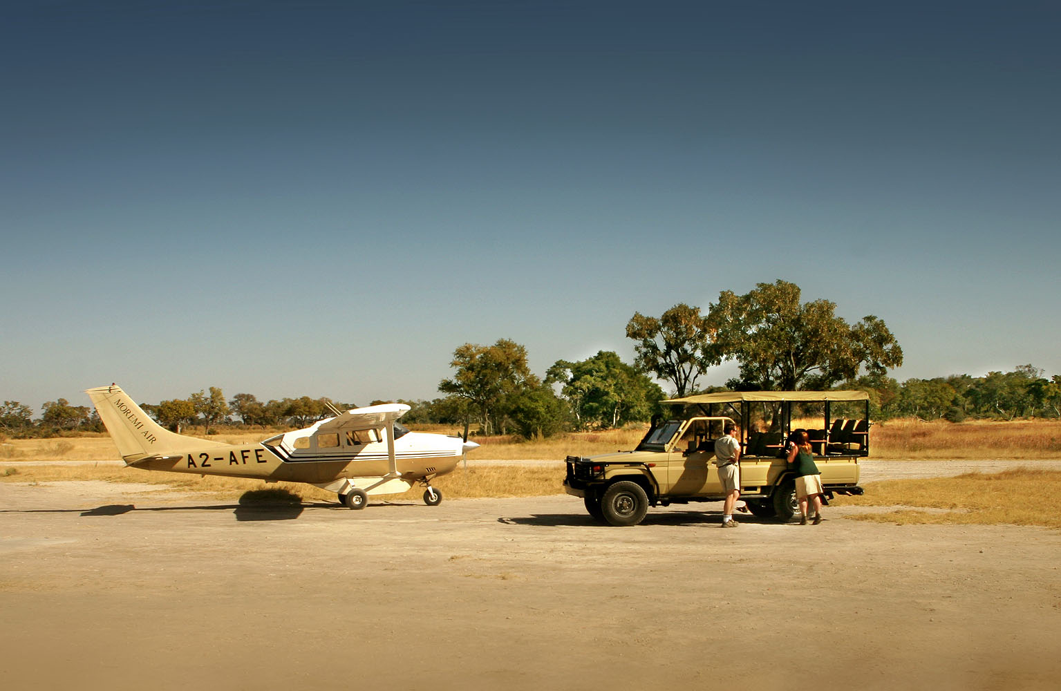 Kleines Buschflugzeug und Safari-Fahrzeug auf einer Landepiste in der Wildnis Botswanas. Reisende wechseln vom Flugzeug in den Geländewagen und beginnen ihre Flugsafari zu den abgelegenen Naturparadiesen des Okavango-Deltas und anderer Schutzgebiete.