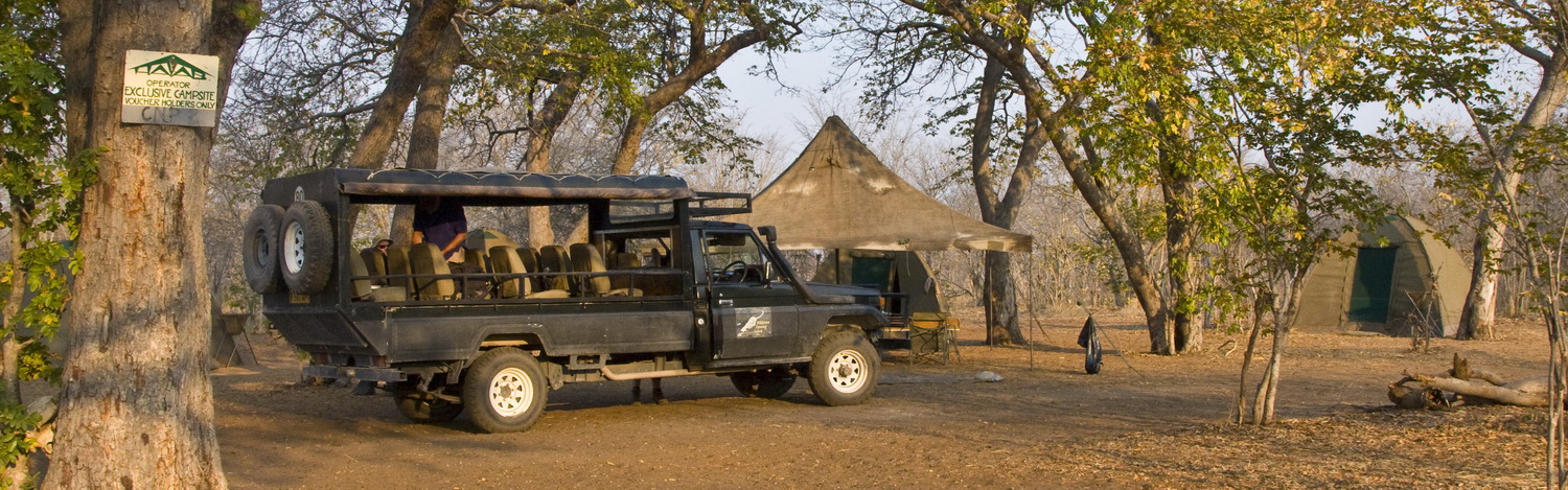 Safari-Fahrzeug in einem naturnahen Zeltcamp in Botswana, umgeben von schattenspendenden Bäumen. Das Camp dient als Ausgangspunkt für Wildtierbeobachtungen und authentische Safari-Erlebnisse in der afrikanischen Wildnis.