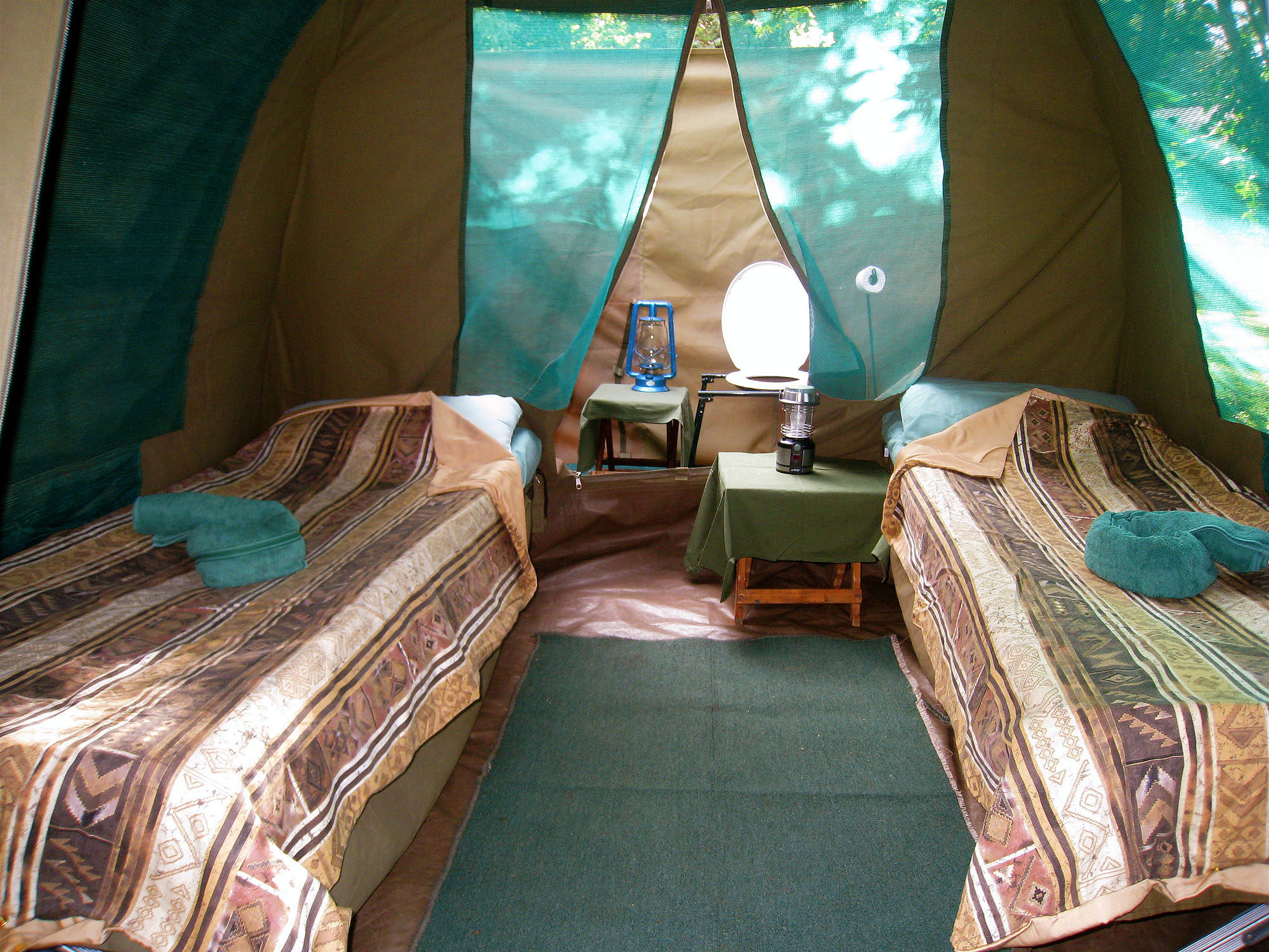 Innenansicht eines komfortablen Safari-Zeltes in Botswana mit zwei Einzelbetten, Nachttischen und Campinglampen. Authentische Zeltcamp-Unterkunft inmitten der afrikanischen Wildnis während einer Safari- und Naturreise durch Botswana.
