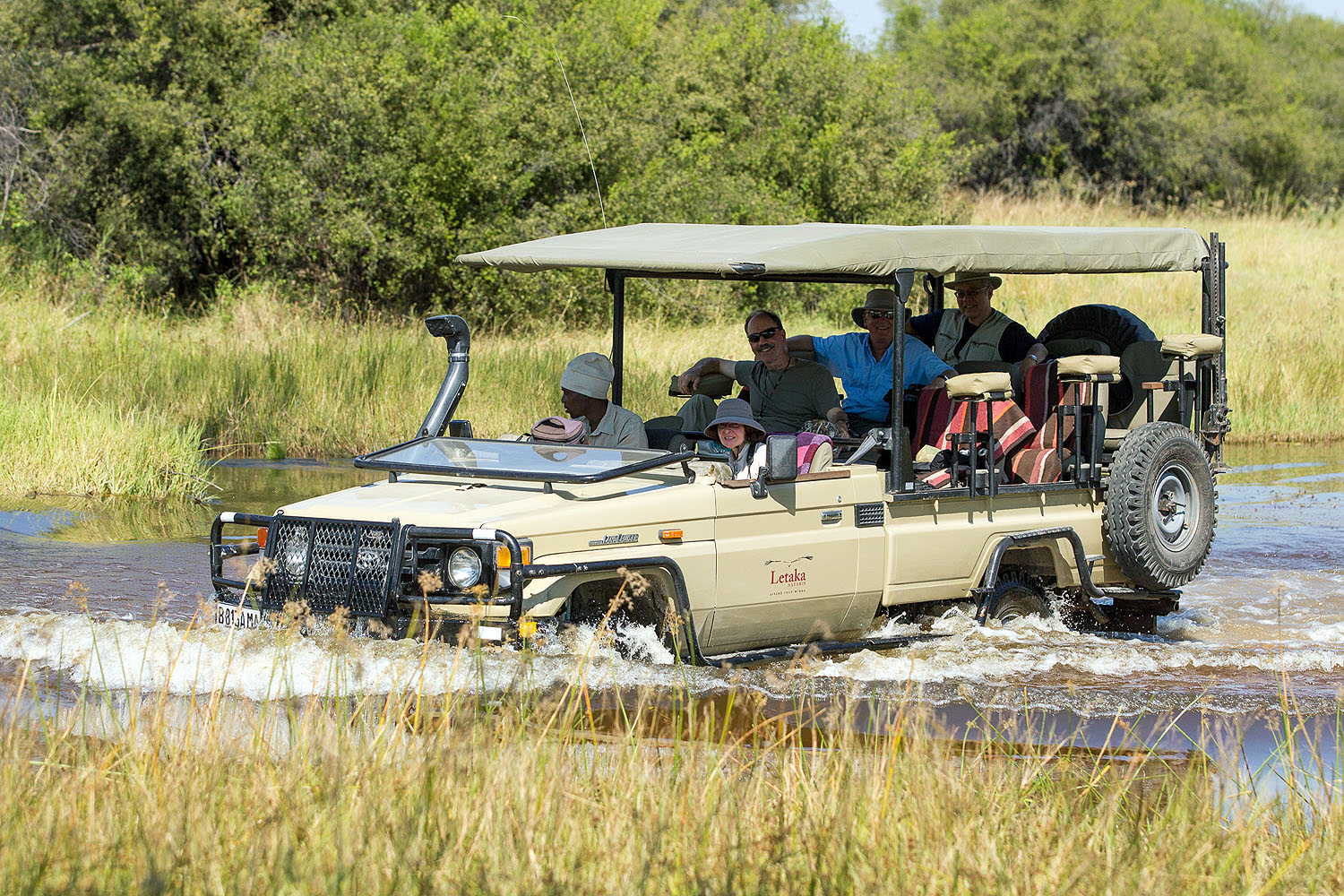 Safari-Gäste in einem Geländewagen bei der Durchquerung einer überfluteten Ebene im Okavango-Delta in Botswana.