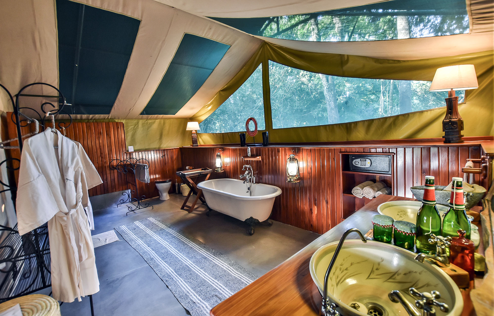 Elegantes Badezimmer in einem Safari-Zelt mit freistehender Badewanne, Doppelwaschbecken und Blick ins grüne Buschland.