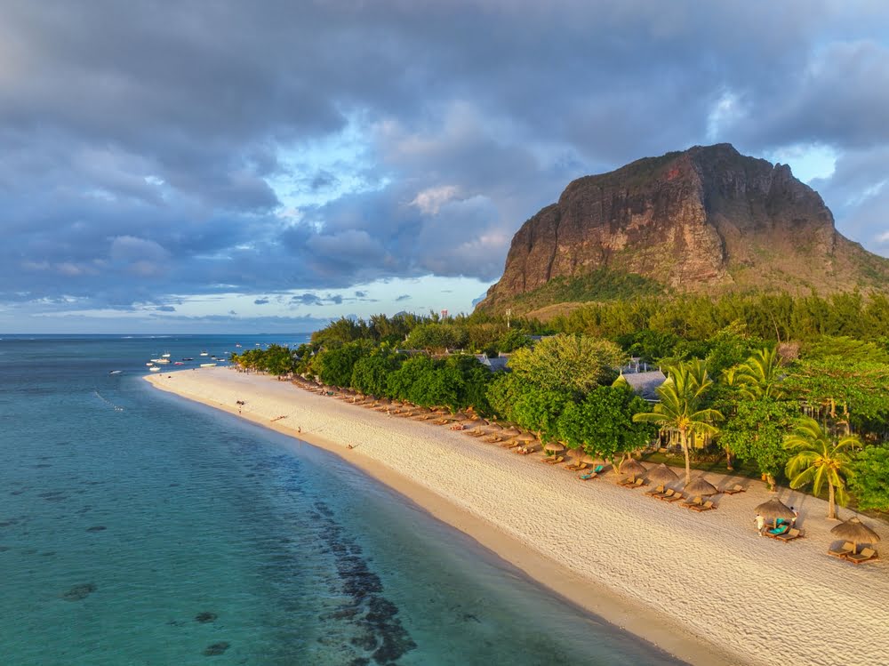 Traumstrand auf Mauritius mit türkisfarbenem Wasser, Palmen und dem markanten Berg Le Morne Brabant im Hintergrund.