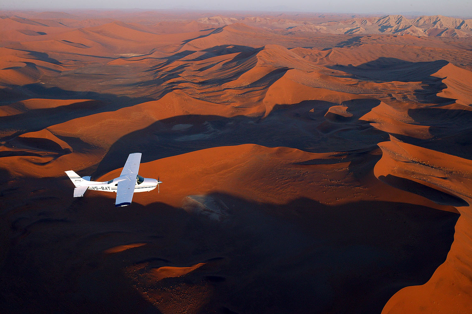 Kleinflugzeug über den roten Sanddünen der Namib-Wüste bei Sossusvlei in Namibia aus der Luft fotografiert.