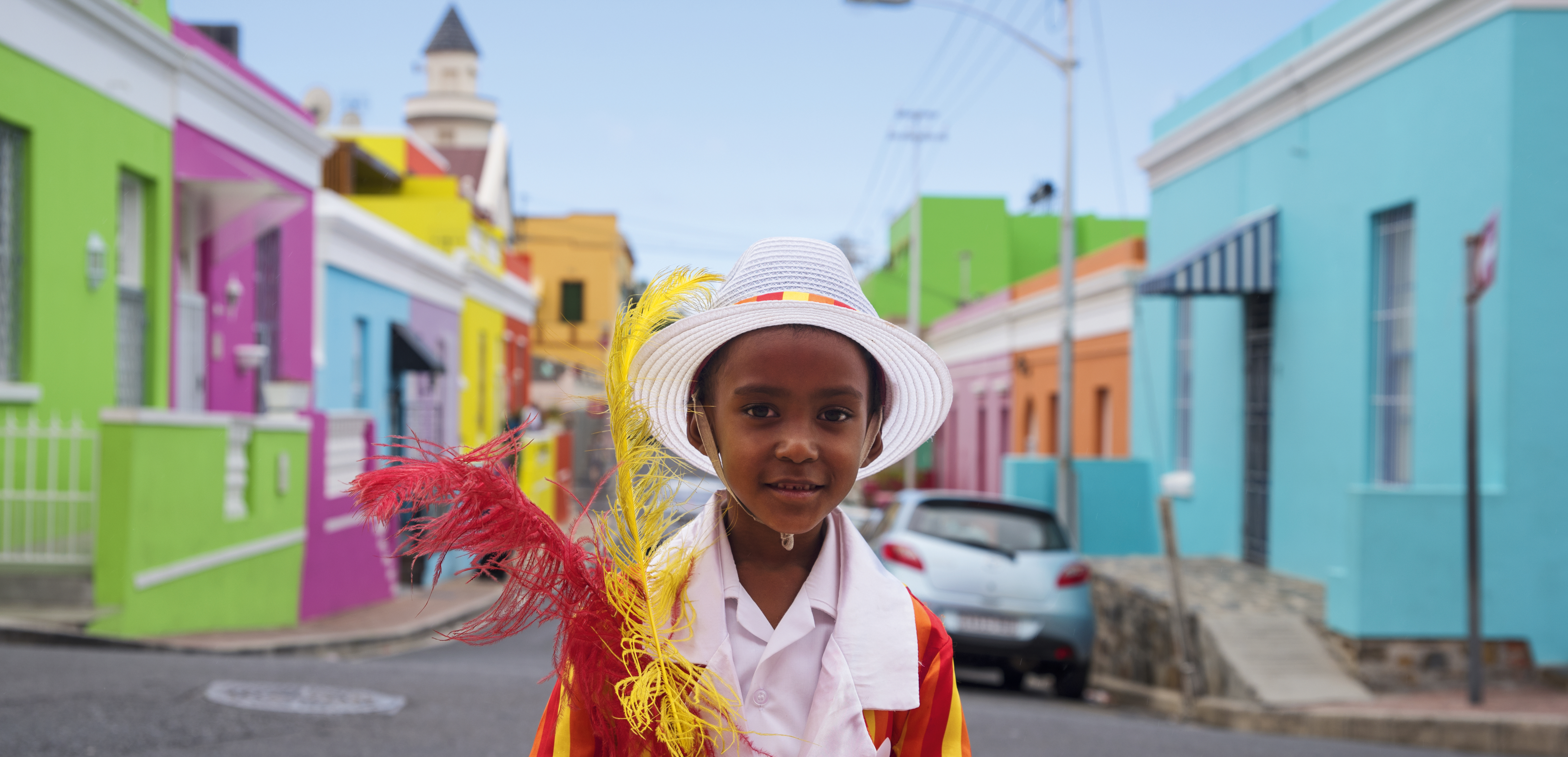Kind in traditioneller Kleidung vor den farbenfrohen Häusern des Bo-Kaap-Viertels in Kapstadt, Südafrika.