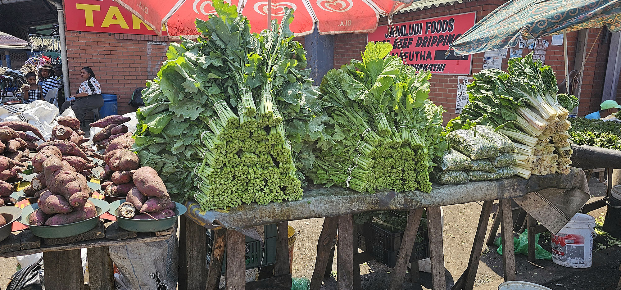 Frisches Blattgemüse und Süßkartoffeln werden auf einem traditionellen Markt in Eswatini angeboten.