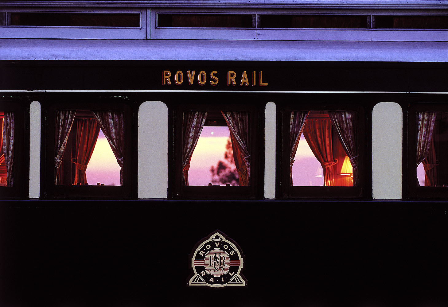 Außenansicht eines Wagens des luxuriösen Rovos Rail in Südafrika mit beleuchteten Fenstern während der Abenddämmerung.