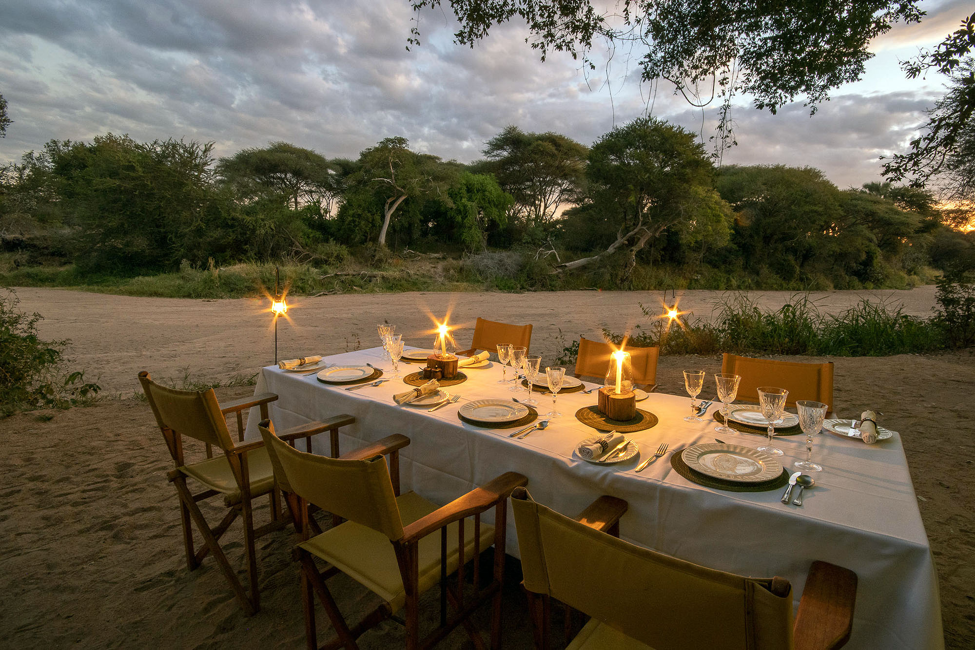 Stilvoll gedeckter Tisch für ein Bush-Dinner in der afrikanischen Wildnis des Nyerere Nationalparks in Tansania bei Sonnenuntergang.