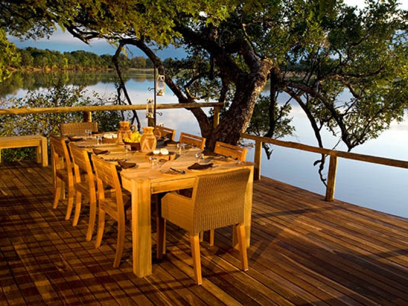 Frühstückstisch auf einer Lodge-Terrasse direkt am Flussufer in Uganda mit Blick auf die unberührte Natur.